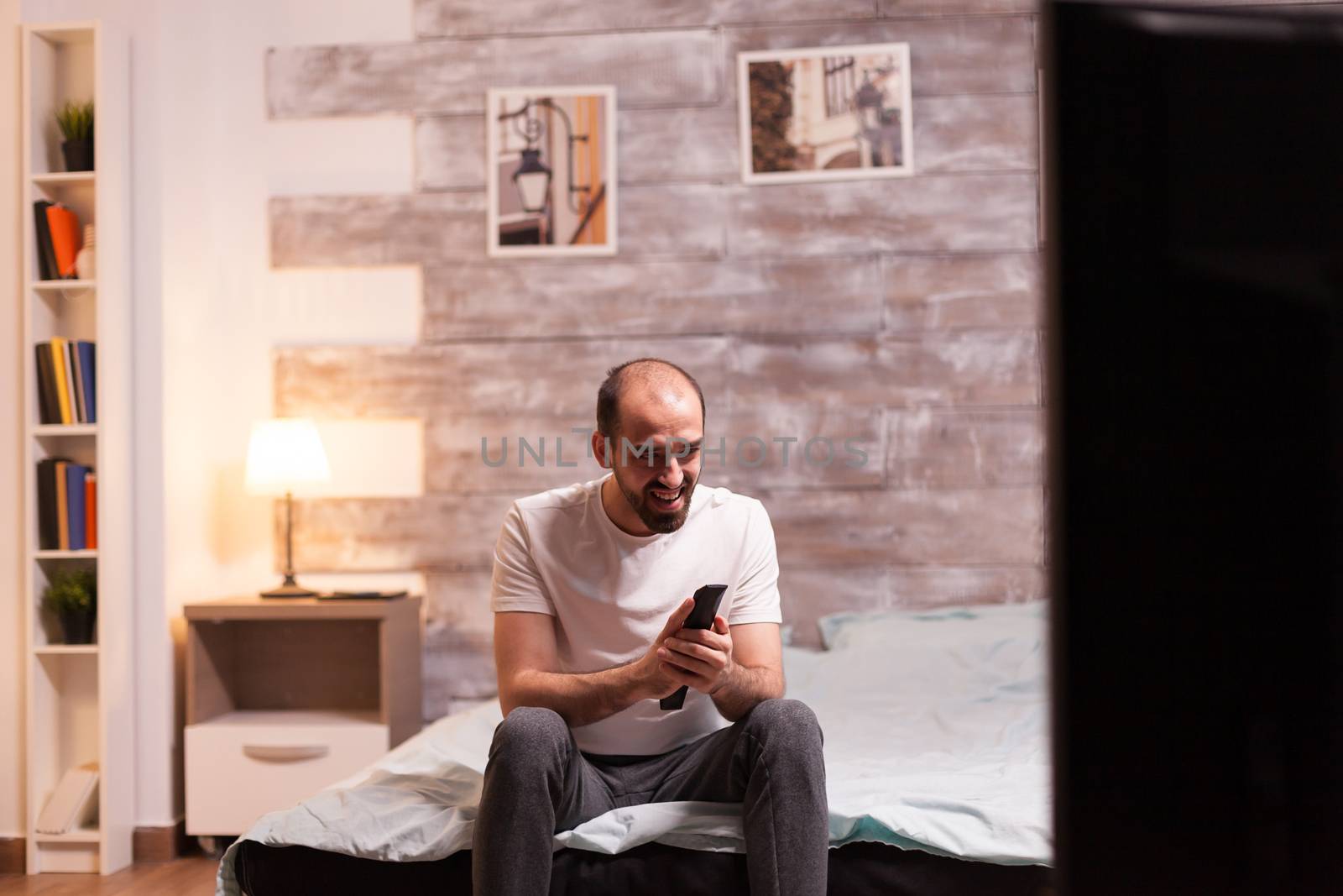 Man at night in pajamas laughing while watching a movie on tv.