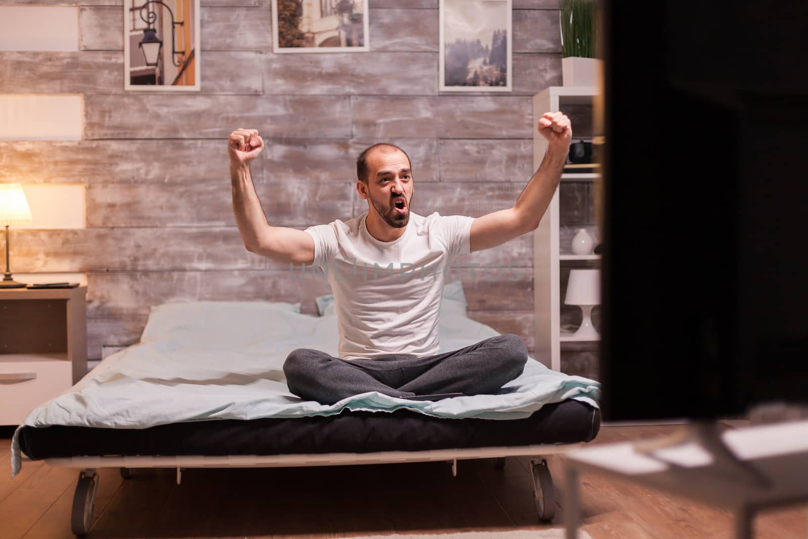 Excited young man sitting on the edge of the bed by DCStudio