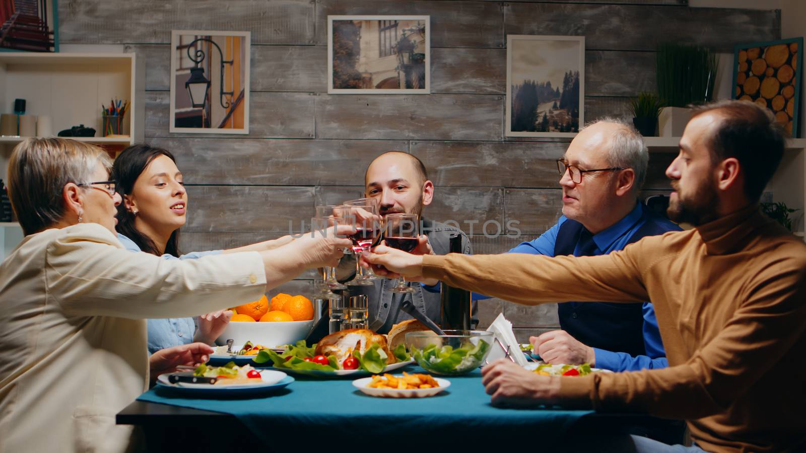 Mother and father in their sixties clinking glasses of red wine with their children at family dinner.