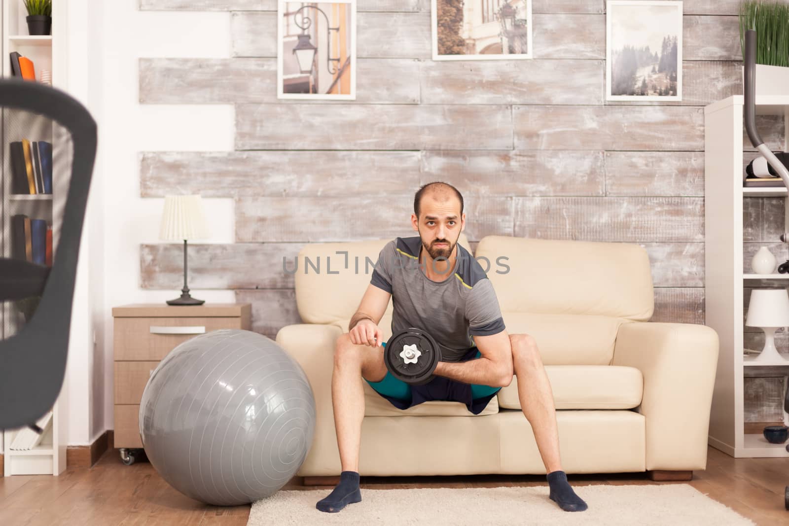 Athletic man using dumbbells to train biceps at home during covid-19 self isolation.