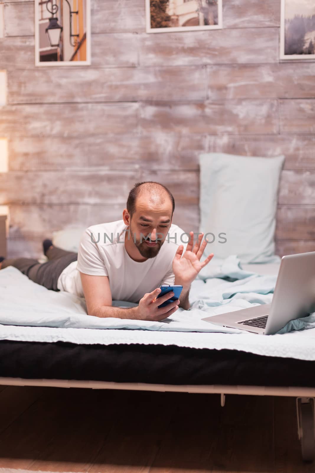 Man at night in bed during a video call waving laying in comfortable bed.