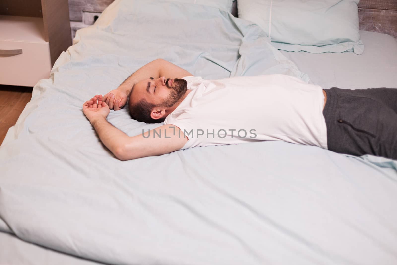 Tired man laying on comfortable bed with eyes closed.