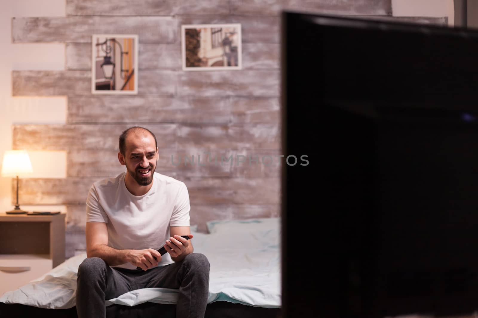 Man relaxing watching tv wearing pajamas at night. Holding remote control.