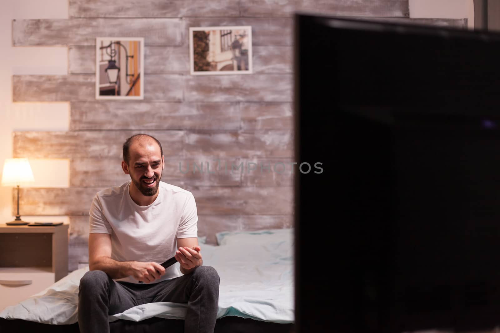 Cheerful man holding remote control watching tv at night.