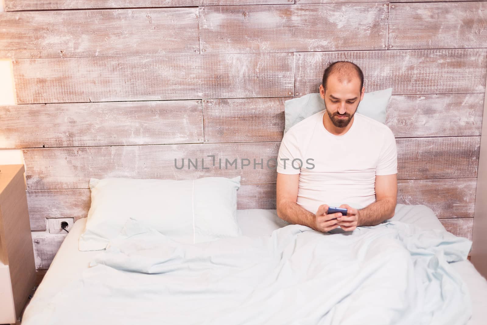 Relaxed man at night using his mobile phone laying in bed.