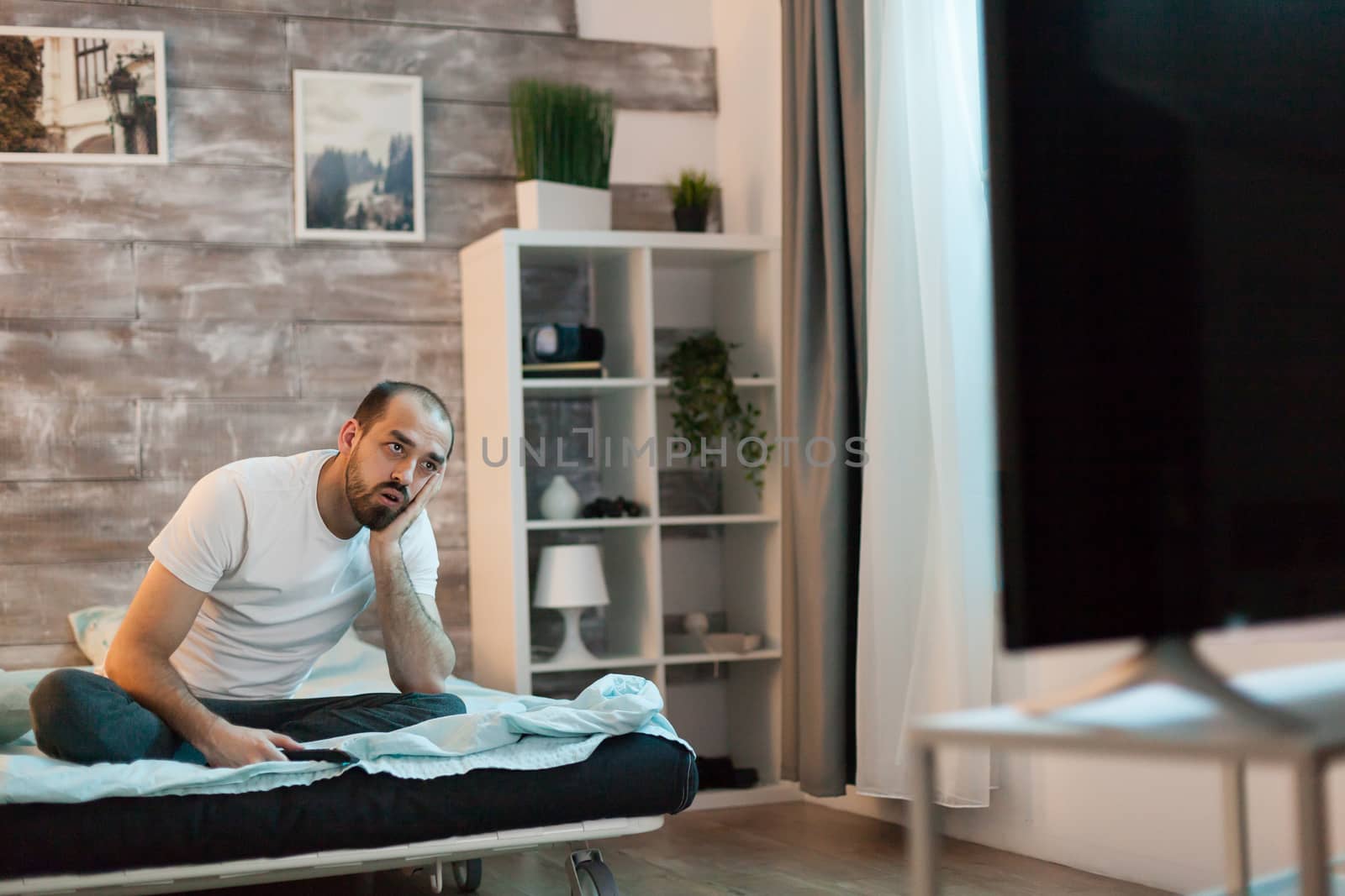 Bearded man watching tv late at night holding remote control.