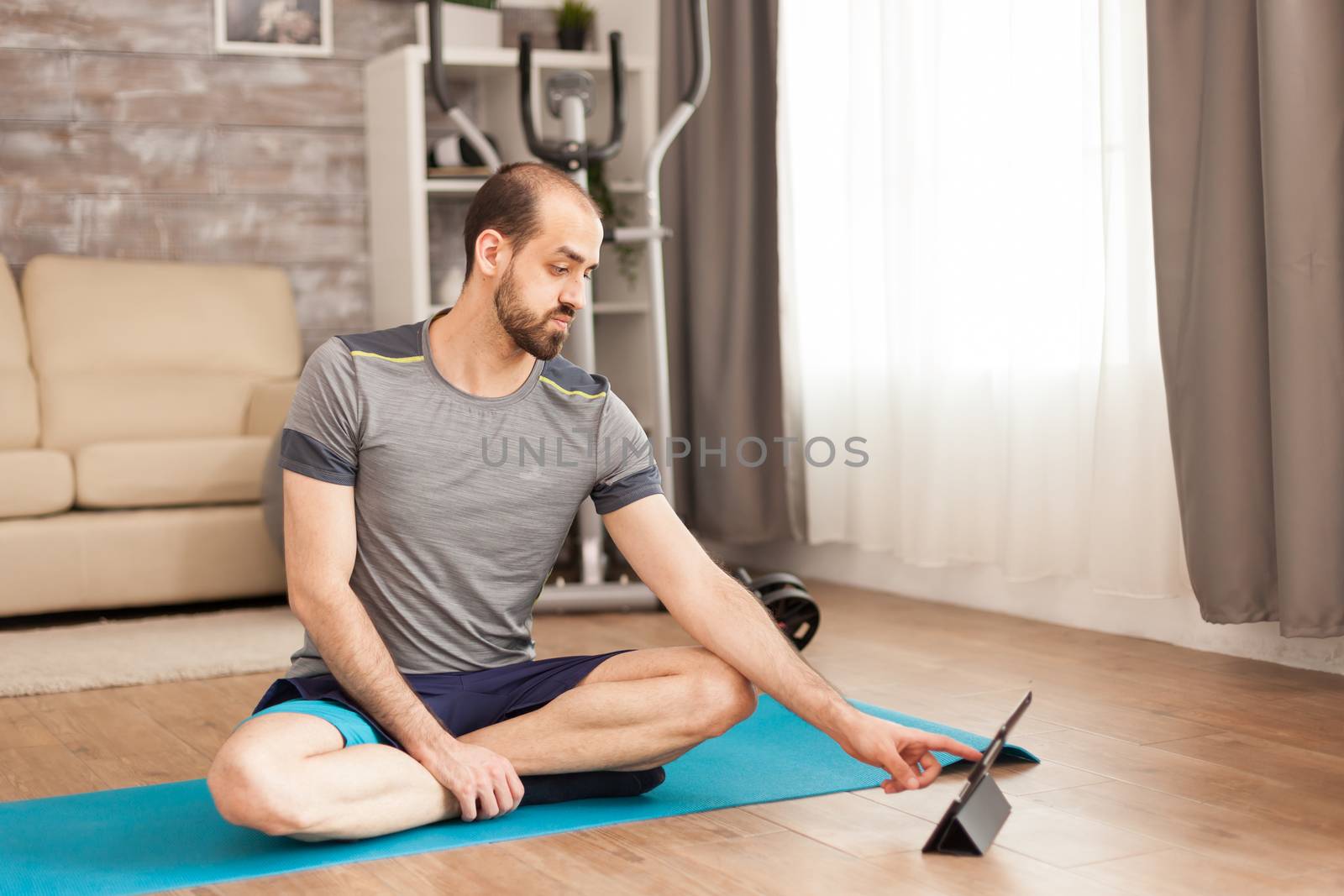 Happy man with healthy lifestyle watching yoga class on tablet computer during covid-19 self isolation.