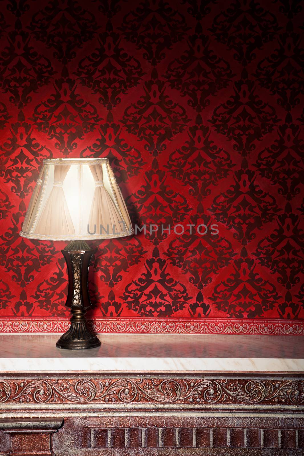 Vintage lamp on old fireplace in room with red rocco pattern. Luxury rocco interior
