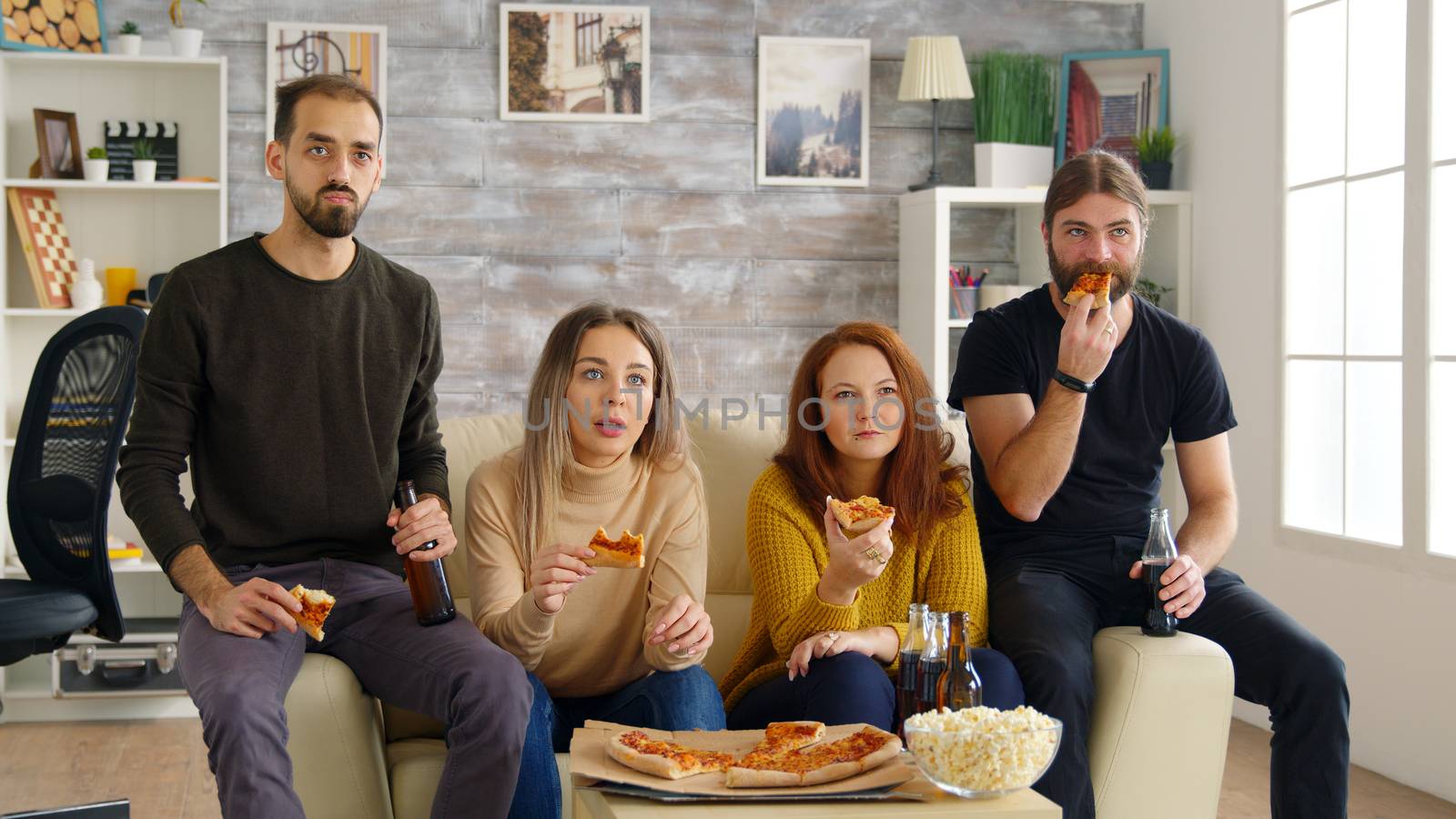 Young man and woman cheering up for their friends while playing video games sitting on couch. Pizza and popcorn.