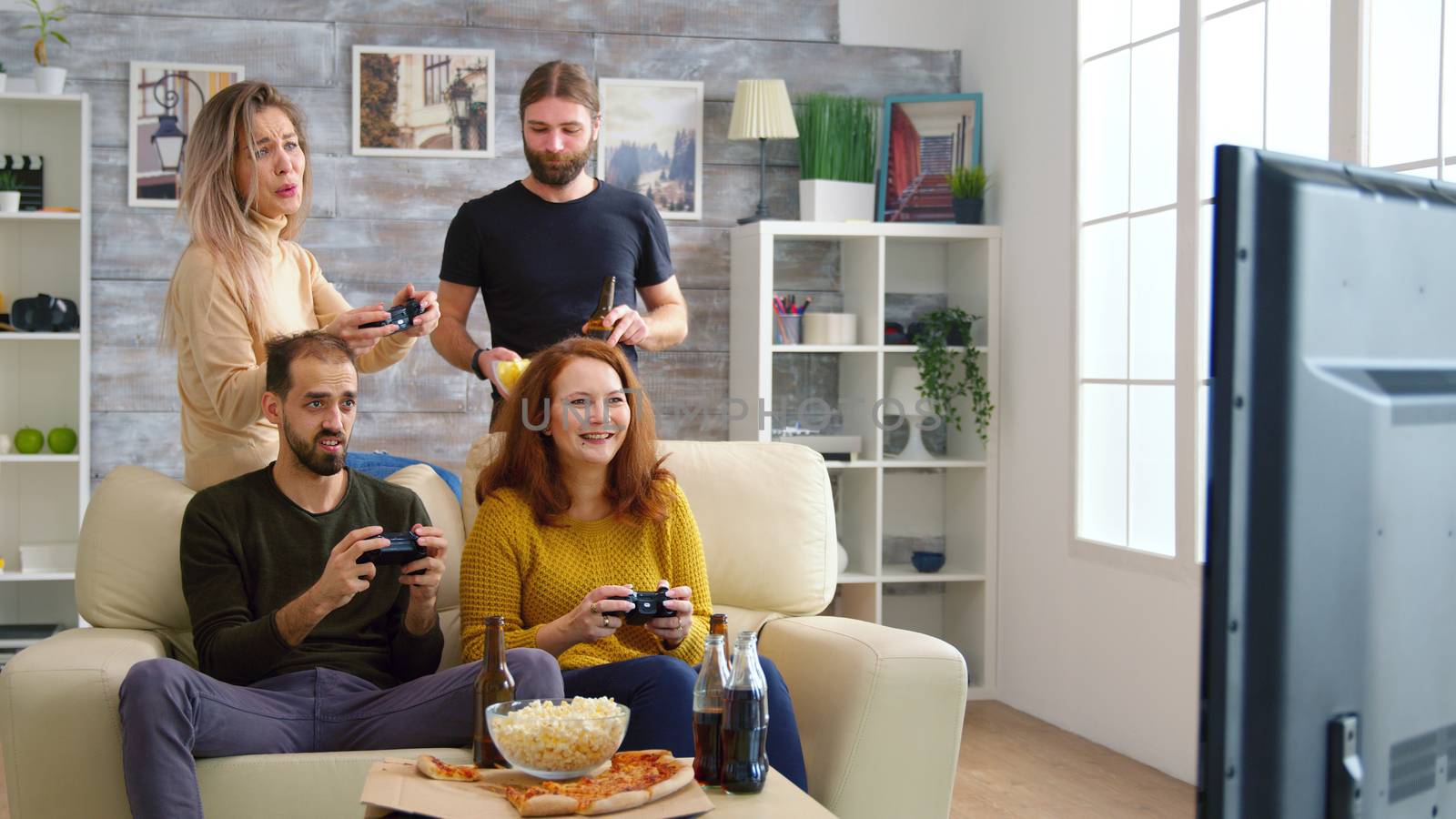 Cheerful caucasian friends playing video games on big tv in living room.