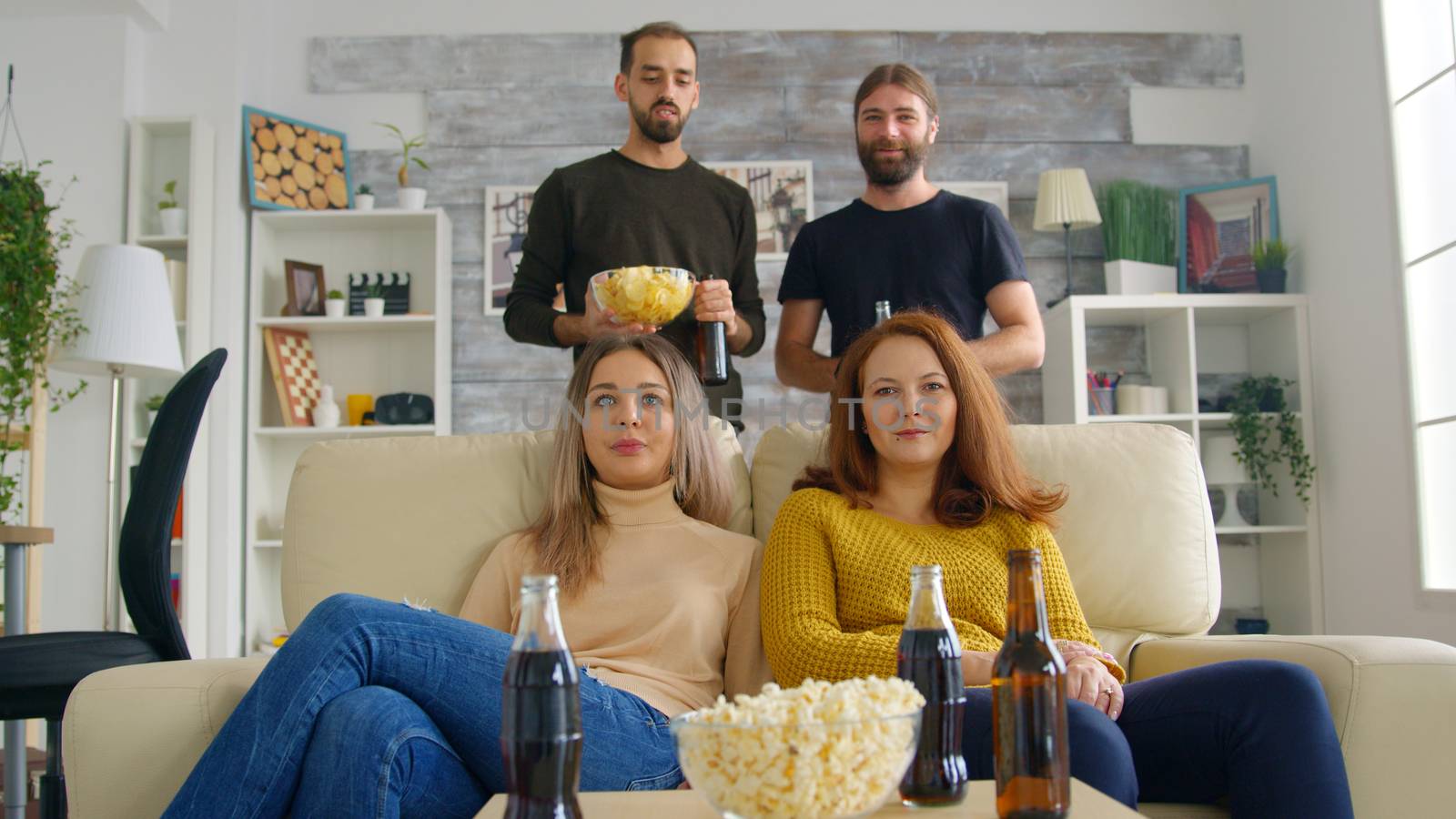 Young woman arriving with pizza to watch a football match on tv with her friends. Happy friends