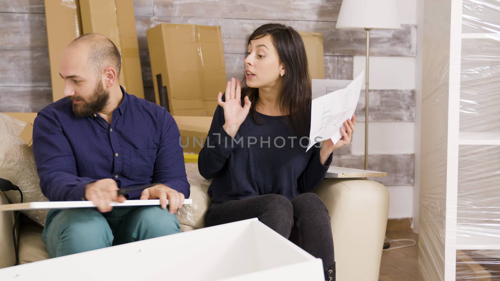 Young couple arguing while assembling furniture in their new apartment. Couple reading instructions.