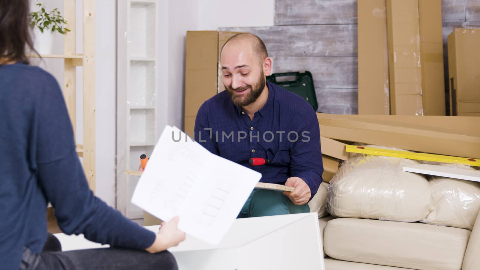 Confused young couple while assembling furniture in their apartment. Girlfriend reading instructions.