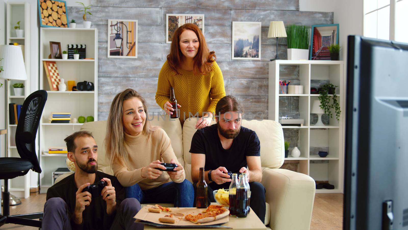 Cheerful caucasian friends playing video games on big tv in living room.