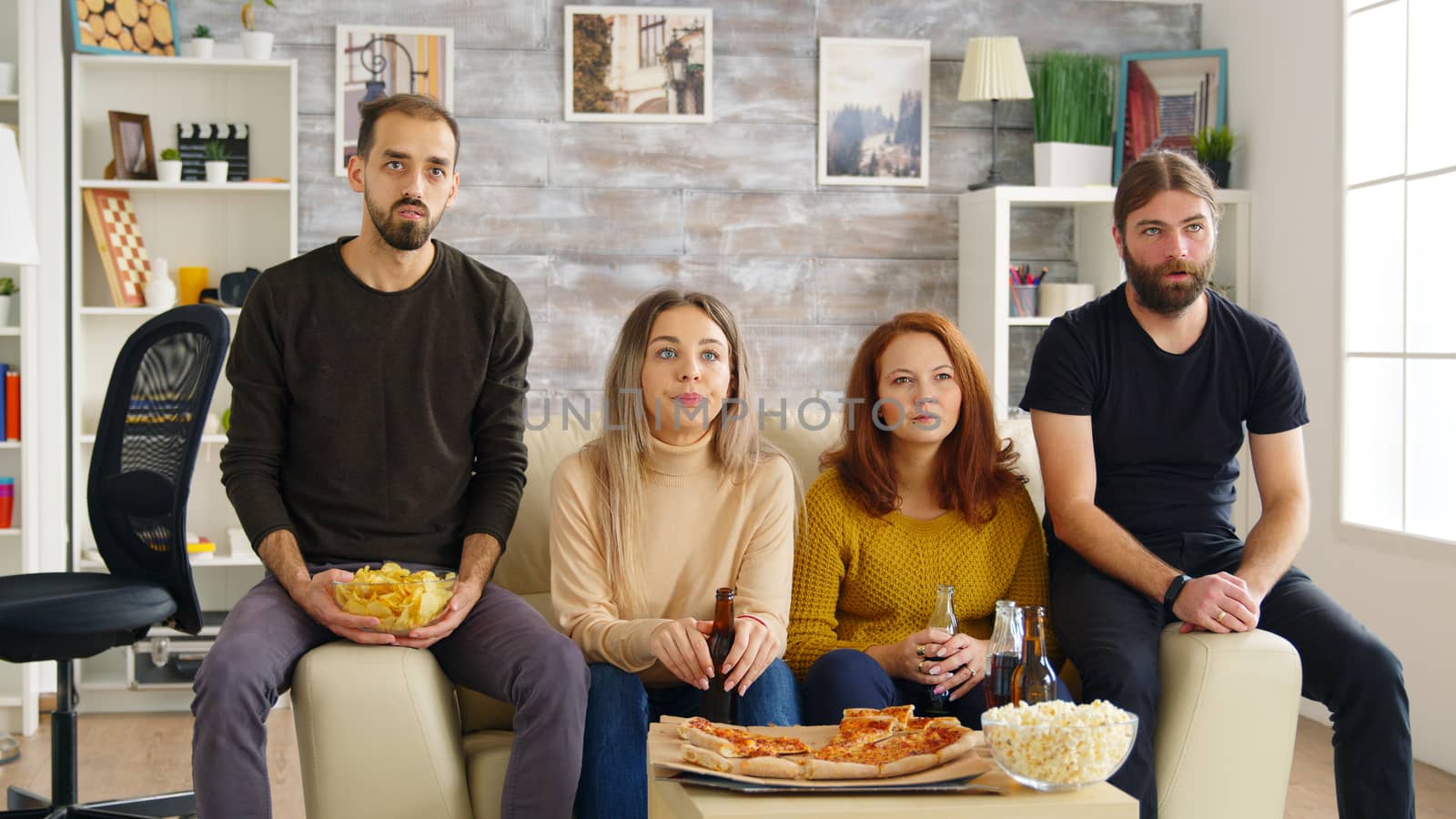 Young man clapping while watching a movie with his friends in living room eating pizza and drinking beer.