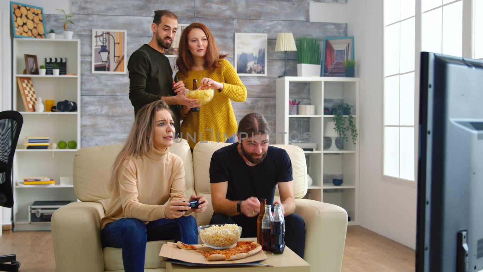 Cheerful caucasian friends playing video games on big tv in living room.