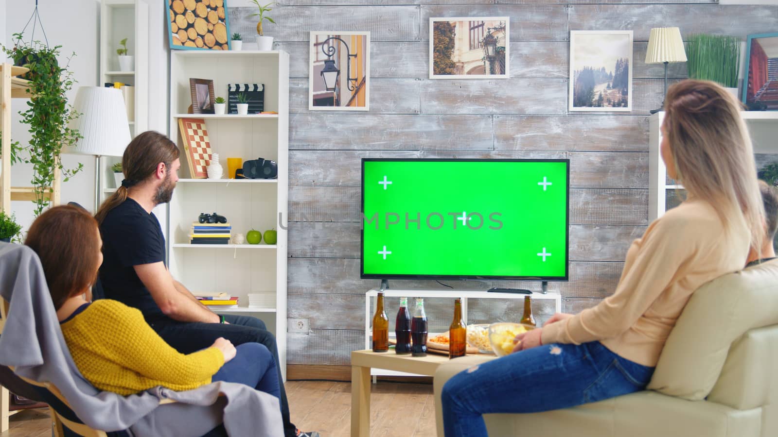 Back view of friends drinking beer and watching sports on tv with green screen in living room.