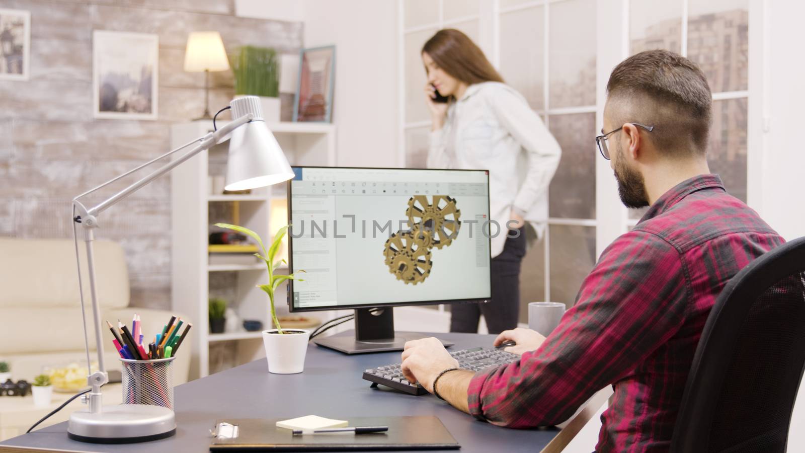 Back view of male engineer working on a mechanical concept from home. Girlfriend in the background.
