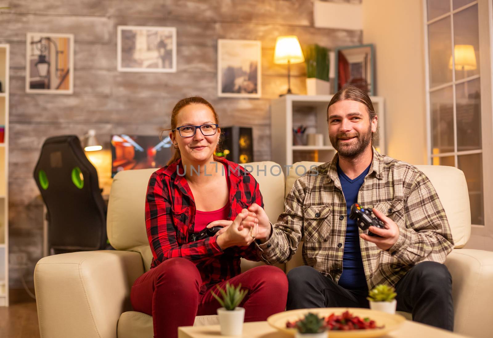 Gamers couple playing video games on the TV with wireless controllers in hands.