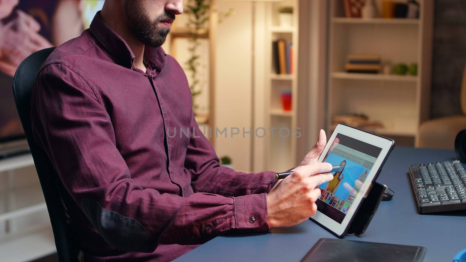Male artist doing skin retouching on tablet computer using a pen at night time.