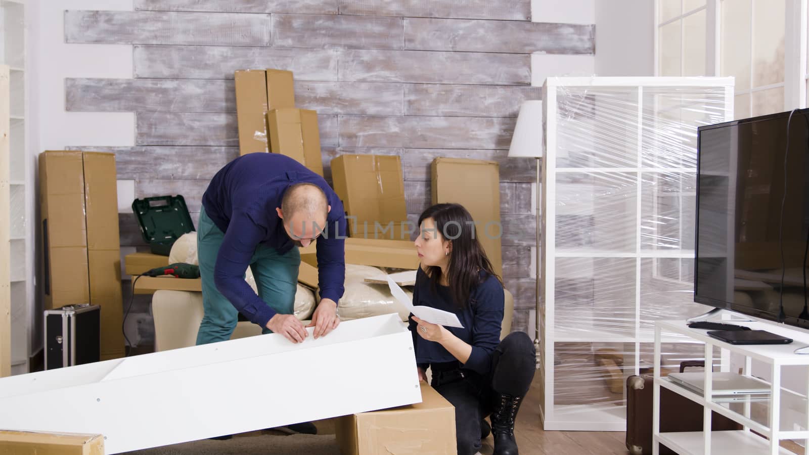 Caucasian young couple in new apartment assembling furniture and reading instructions. Boyfriend using screwdriver. Zoom in shot