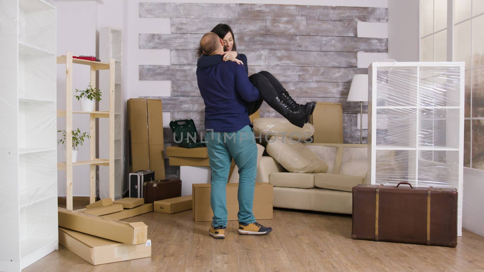 Excited boyfriend spinning his girlfriend in their new apartment. Cheerful young couple.