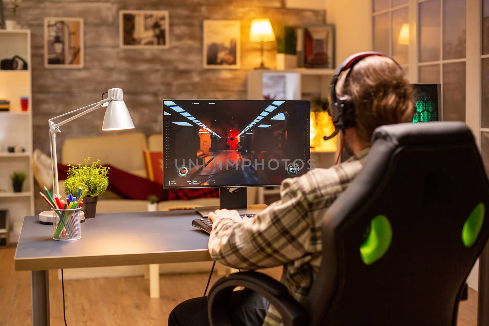 Back view of gamer male playing a shooter on his powerful PC computer late at night in the living room by DCStudio