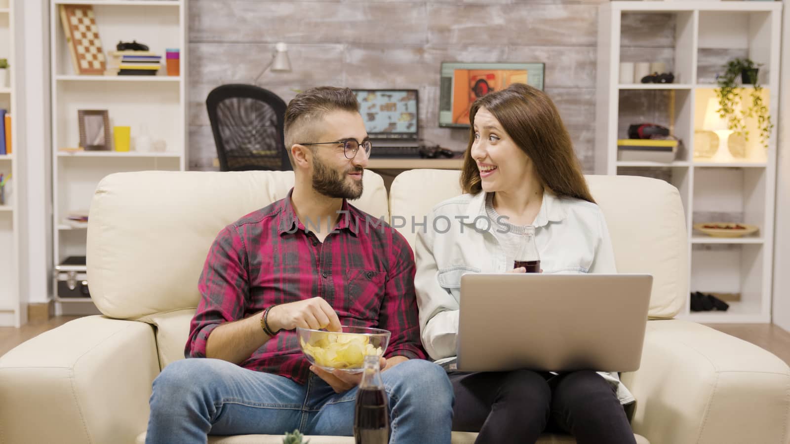 Young couple giving high five while sitting on the couch. Couplea enjoying soda and chips.