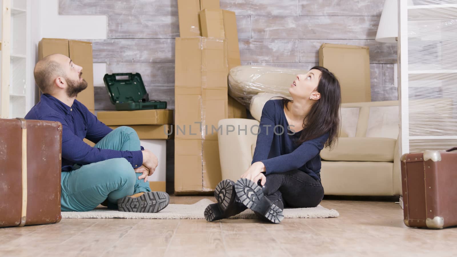 Couple sitting on carpet in their new apartment with suitcases in front of them. Cardboard boxes in the background.