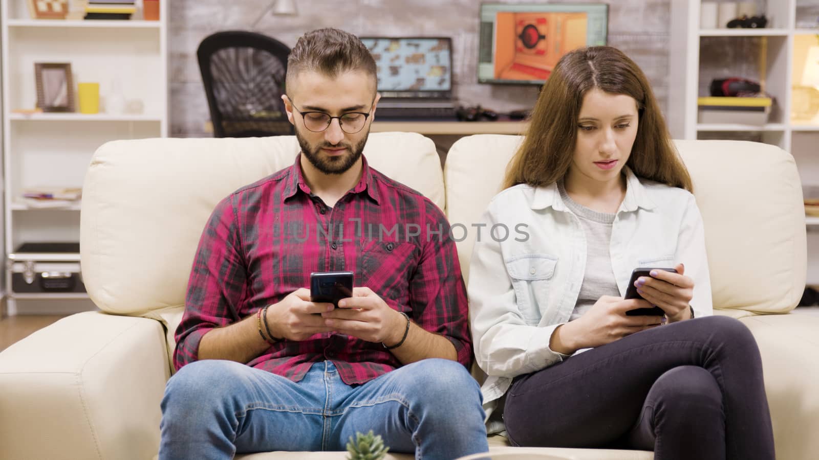 Caucasian couple sitting on the couch browsing on their phones. Boyfriend and girlfriend.
