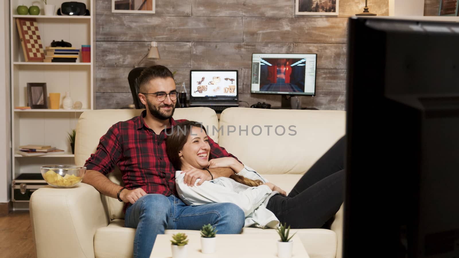 Attractive young couple relaxing on couch while watching a movie on television.
