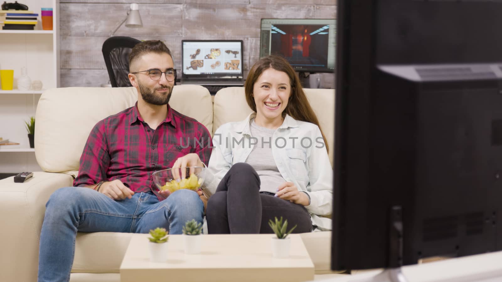 Charming young couple sitting on the couch and watching tv by DCStudio