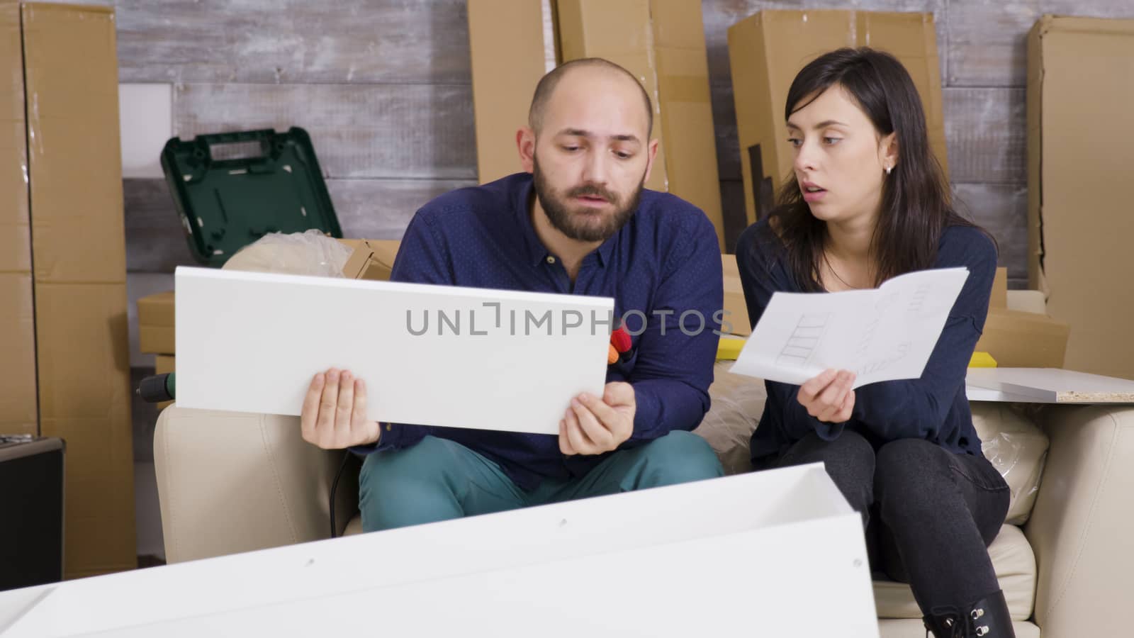 Girlfriend and boyfriend assembling furniture in their new apartment and reading instructions.