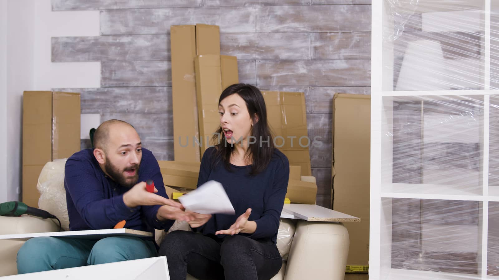Girlfriend hitting boyfriend with instructions while assembling furniture by DCStudio