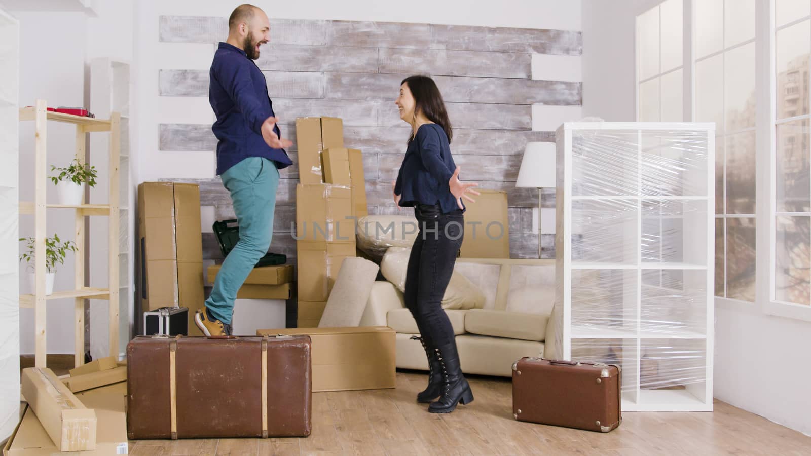 Happy young couple jumping in their new apartment. Excited about their new apartment. Suitcases in apartment.