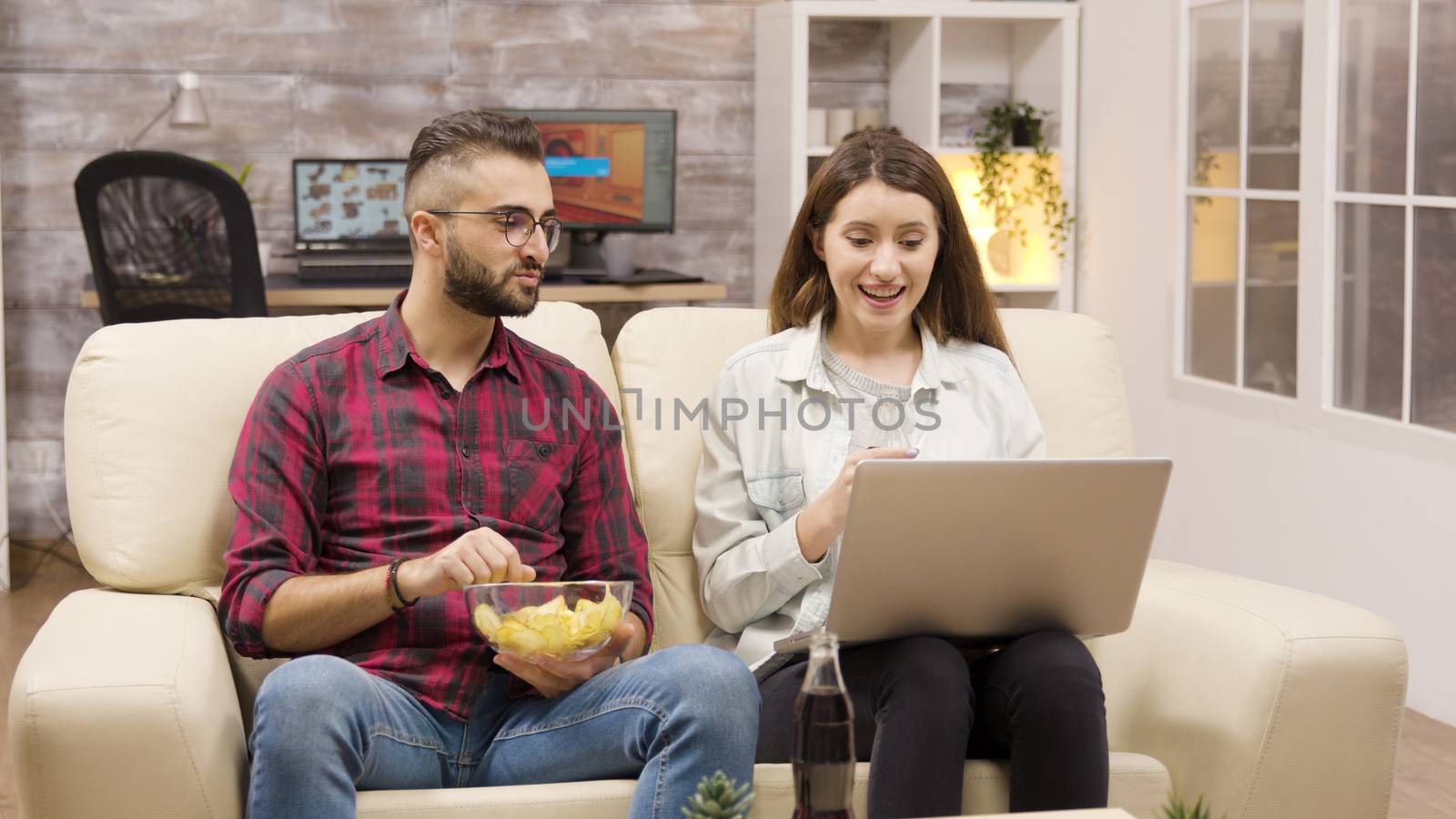 Happy couple on the couch eating chips by DCStudio