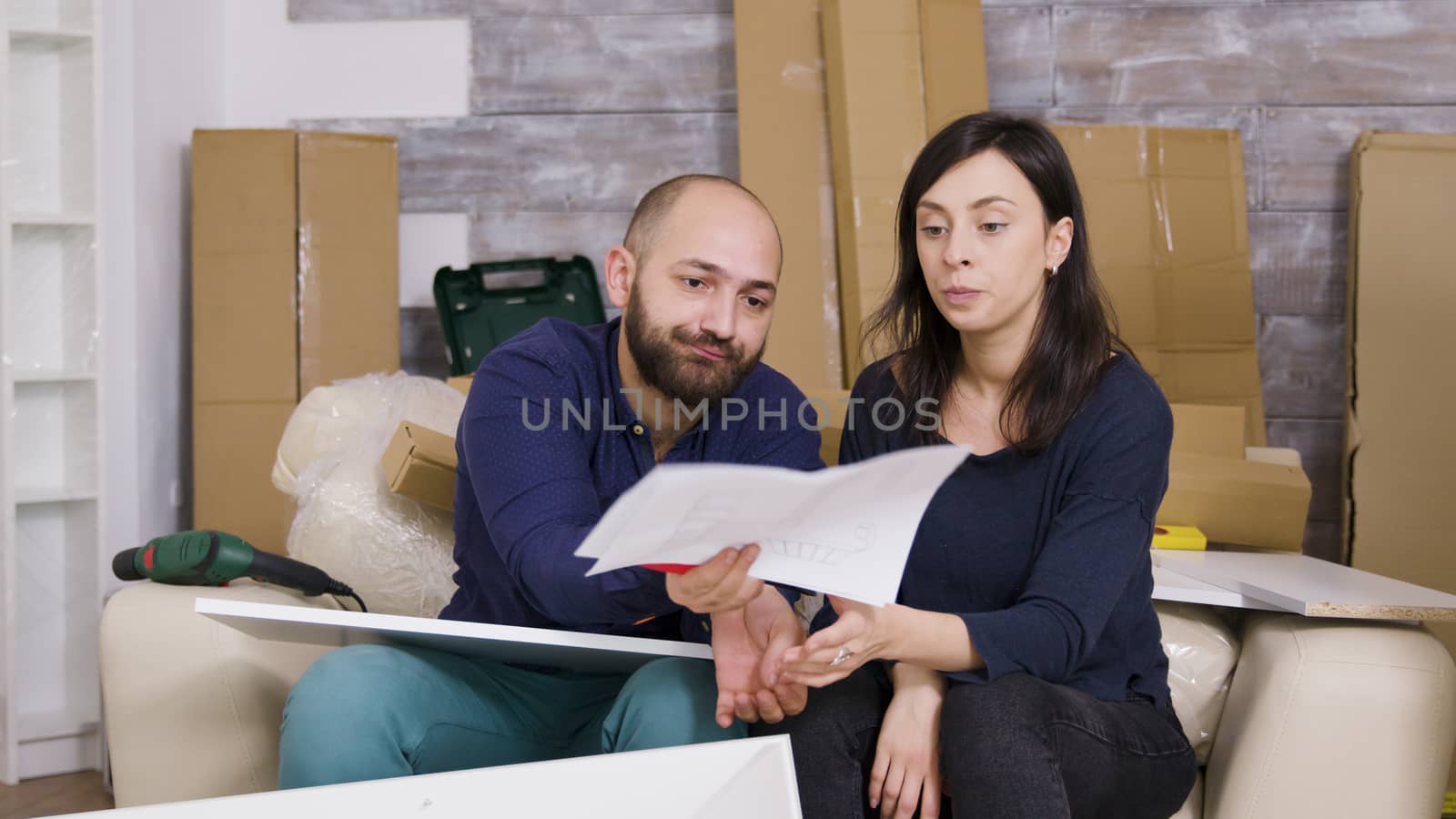 Angry girlfriend hitting boyfriend with furniture instructions. Couple assembling furniture in new apartment.