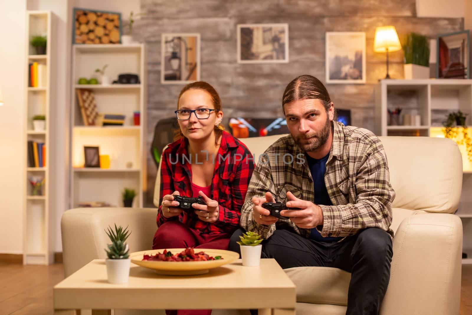 Gamers couple playing video games on the TV with wireless controllers in hands.