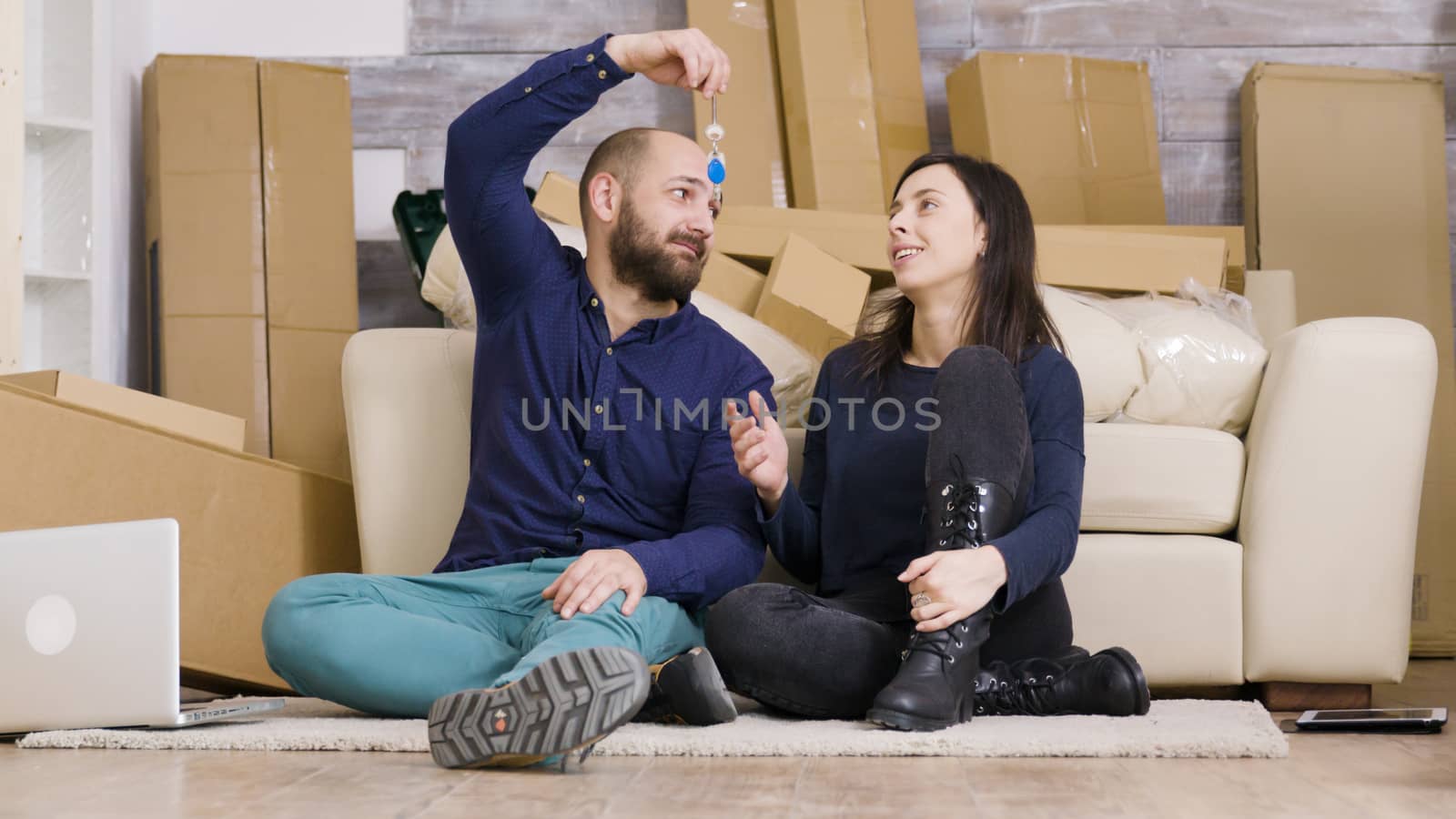 Beautiful young couple sitting on the floor of their new apartment. Boyfriend giving keys to her girlfriend. Cardboard boxes.