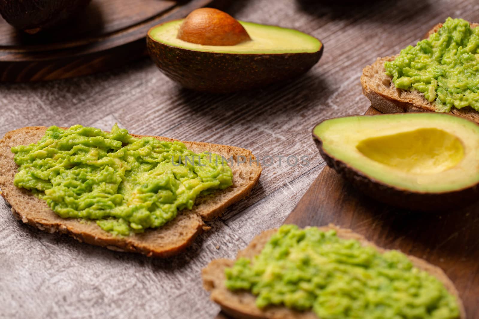 Avocado sandwiches next to cutted ones on wooden board.