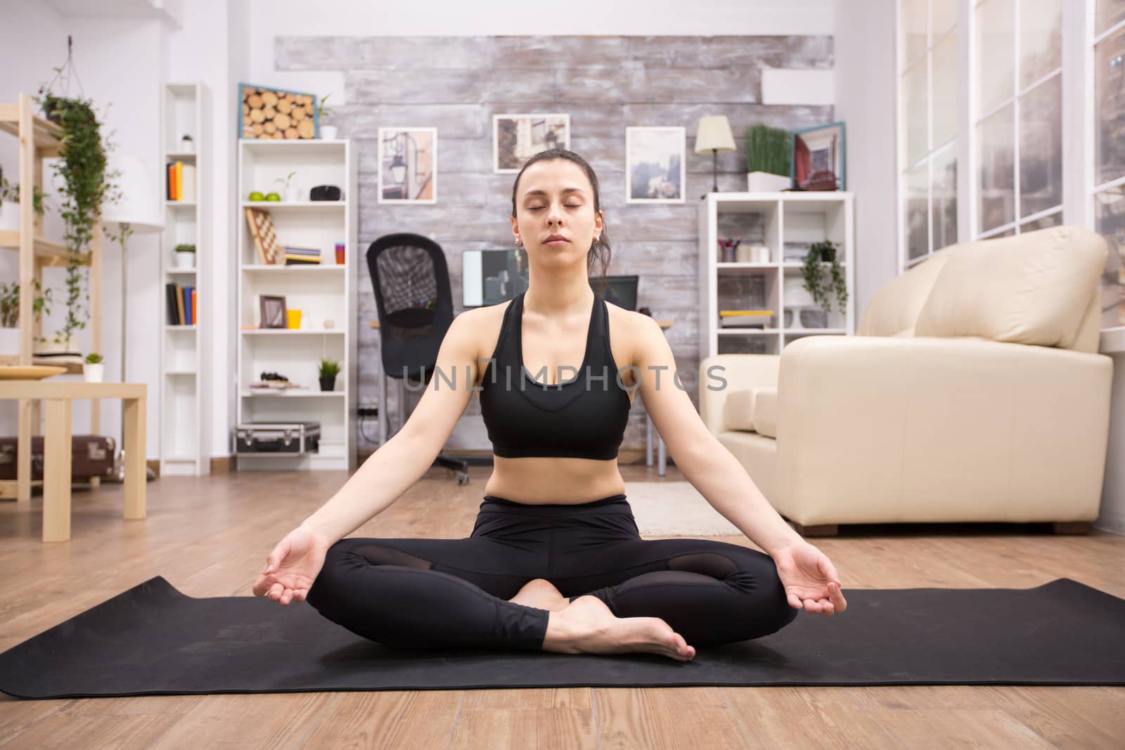 Beautiful adult woman relaxing at home doing yoga lotus pose on the mat.