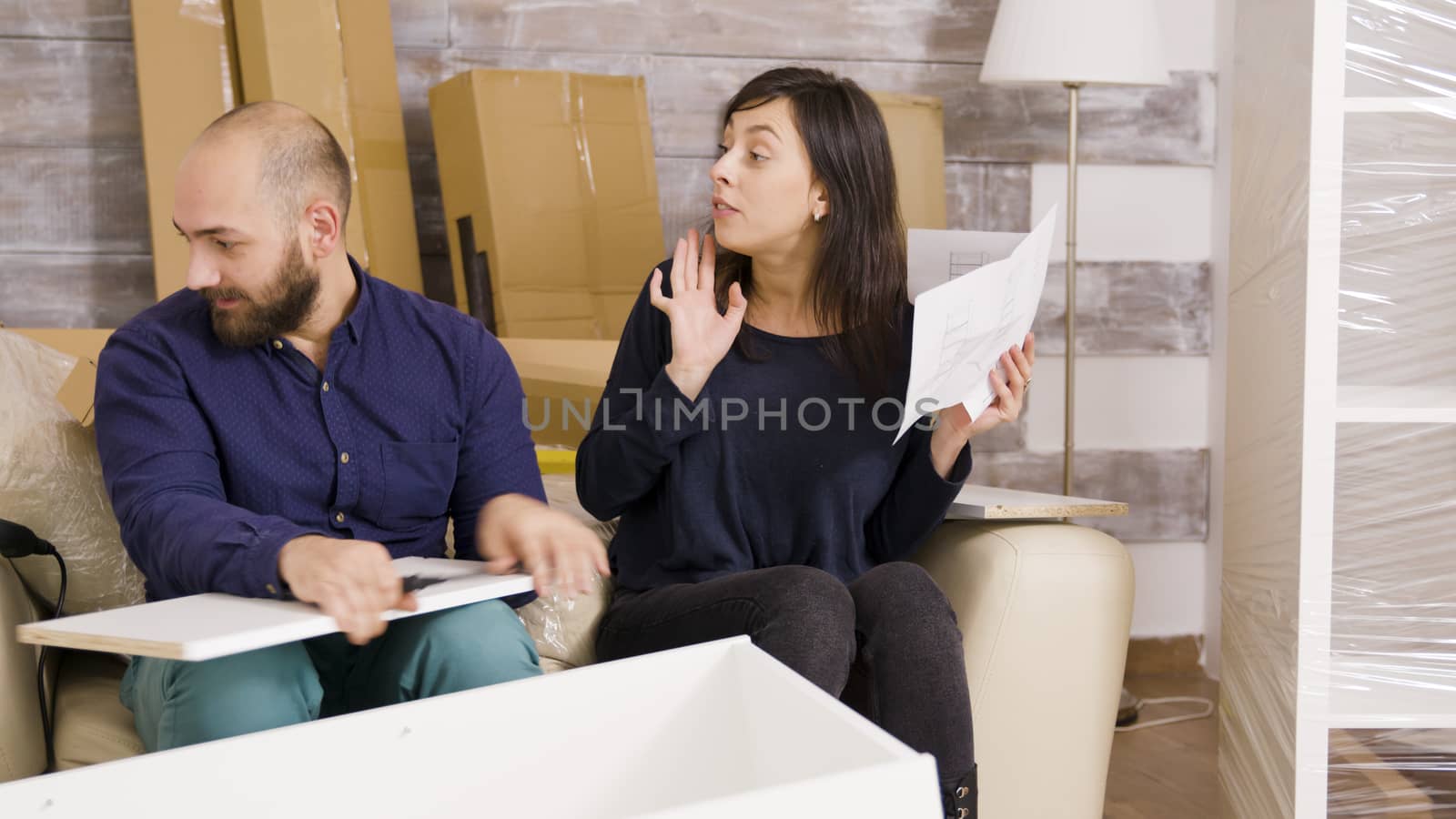 Young couple arguing while assembling furniture in their new apartment. Couple reading instructions.