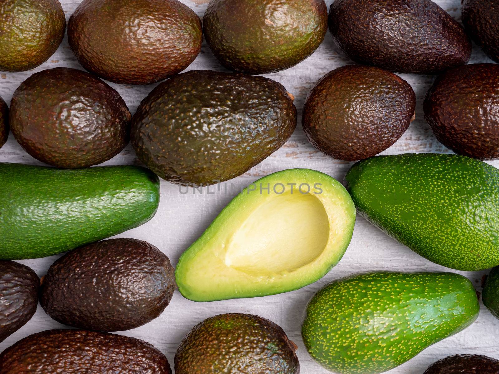 Mix of ripped and green avocados on white wooden board.