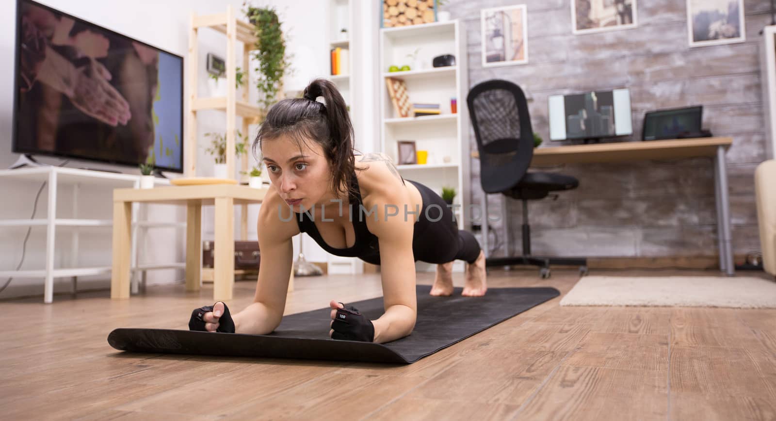Caucasian beautiful woman doing plank training at home wearing black sportswear.