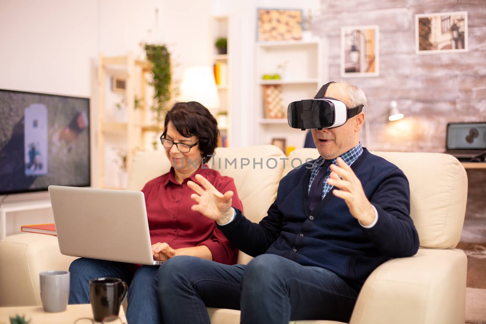 Old elderly retired man using VR virtual reality headset in their cozy apartment.