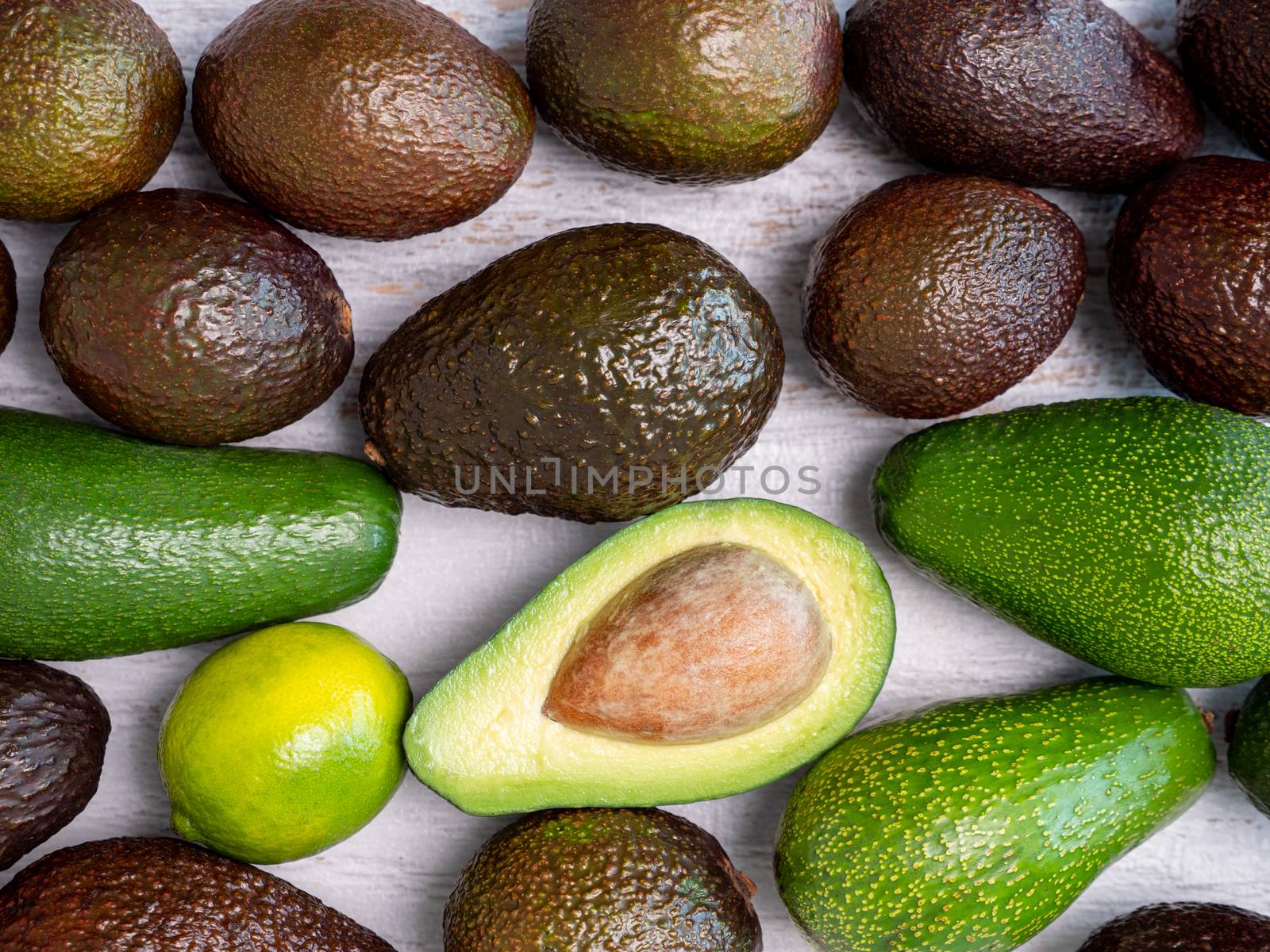 Mix of ripped and green avocados on white wooden board.