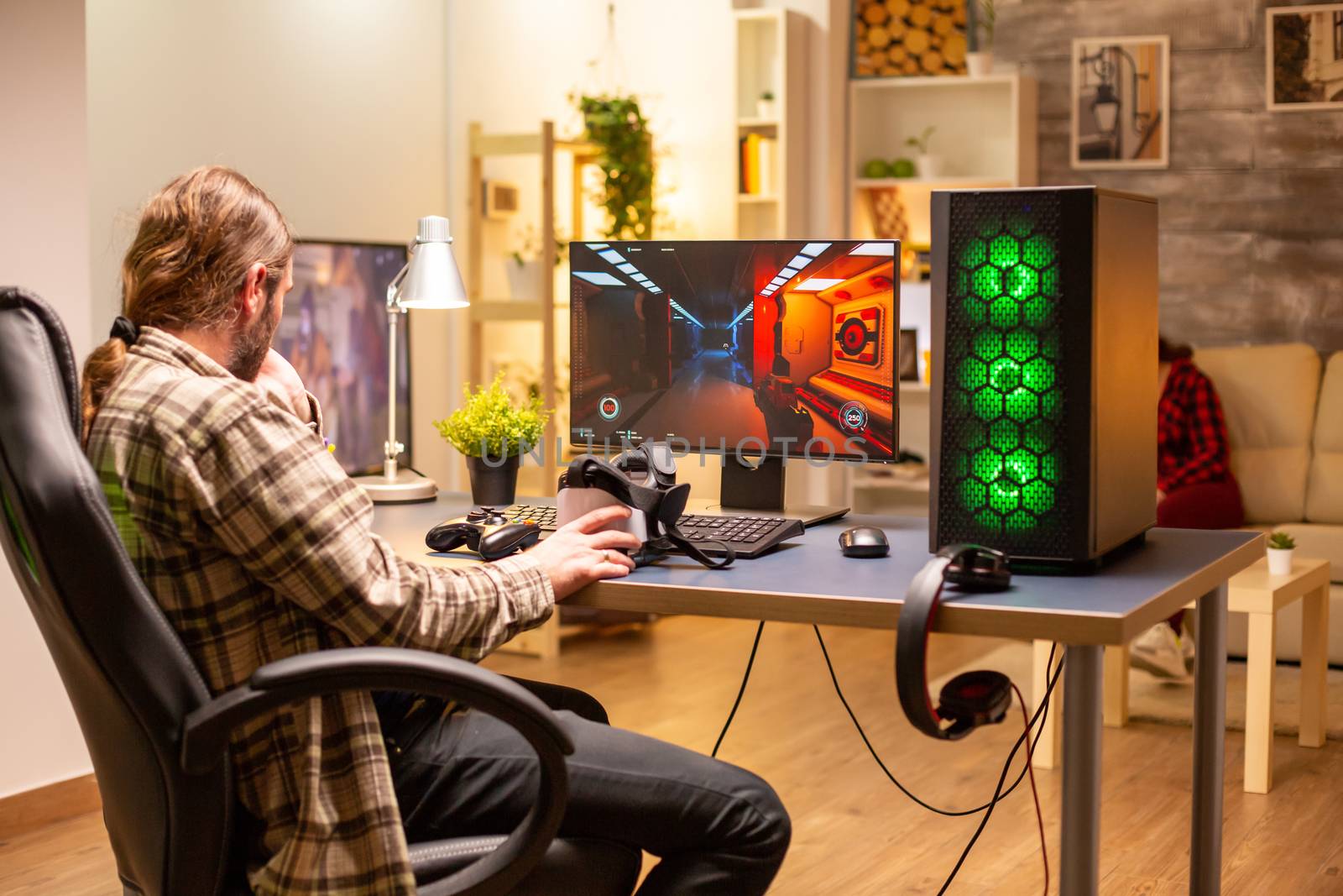 Back view of gamer male playing a shooter on his powerful PC computer late at night in the living room.