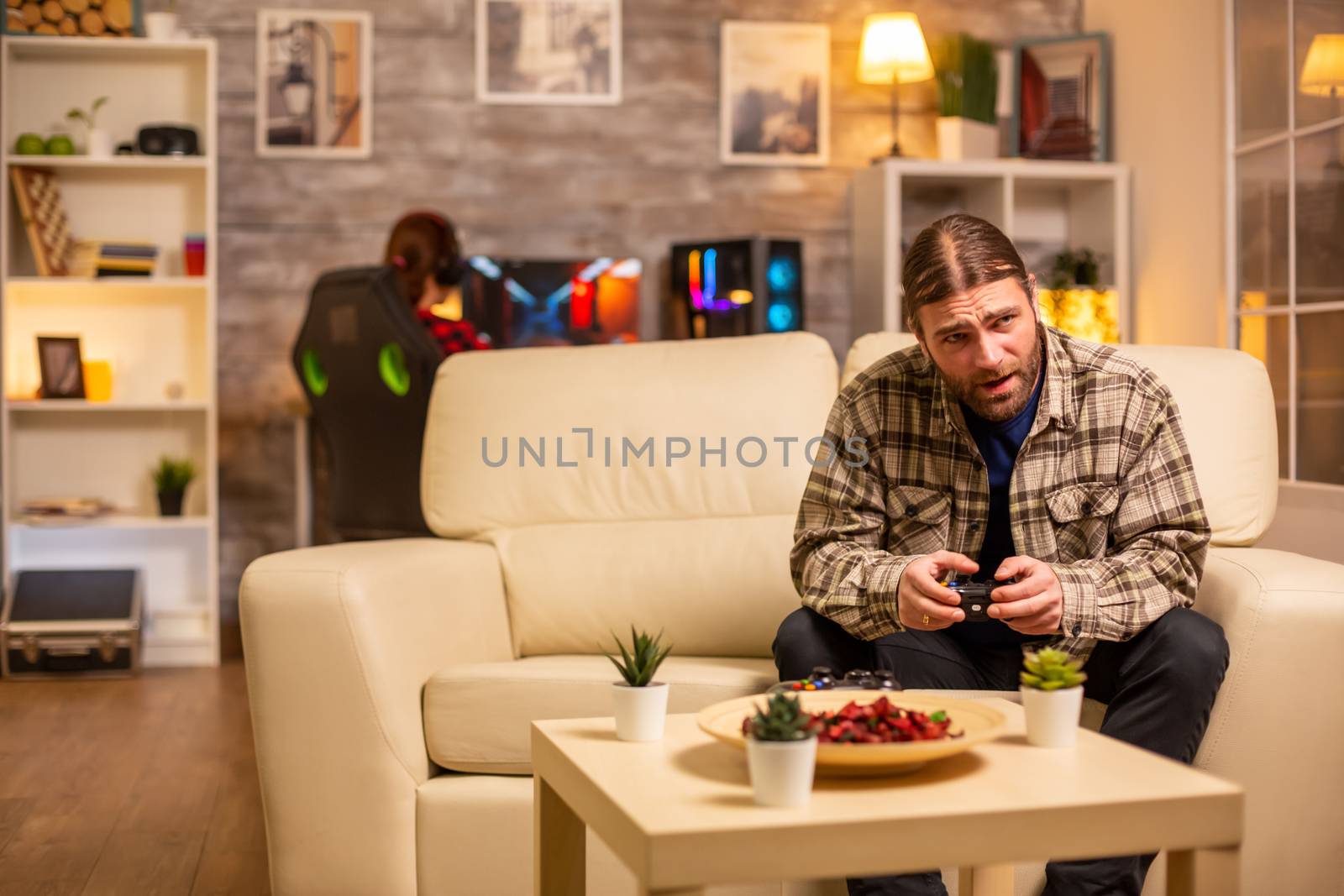 Male gamer playing video games on a console in the living room while sitting on the sofa