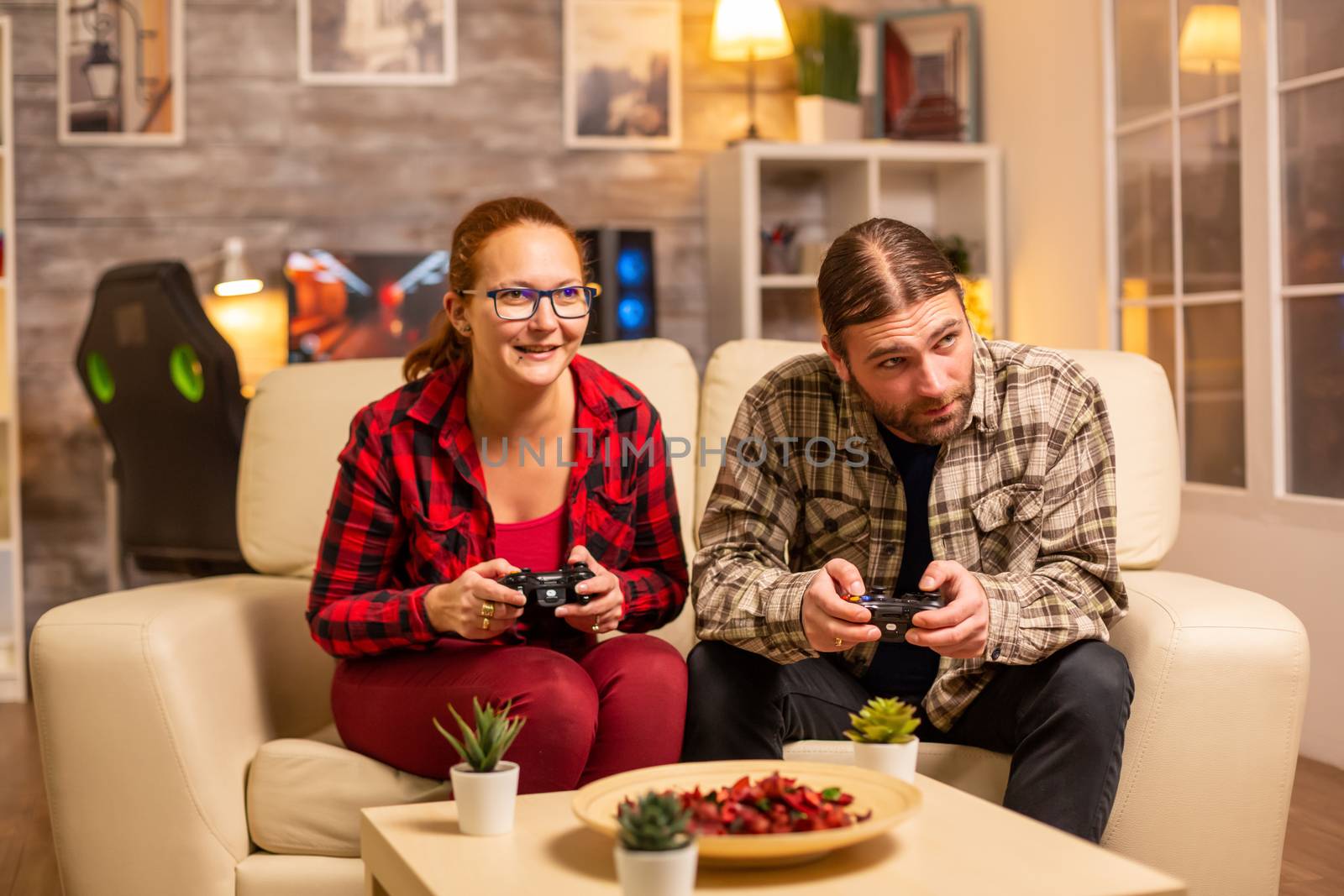 Gamers couple playing video games on the TV with wireless controllers in hands.