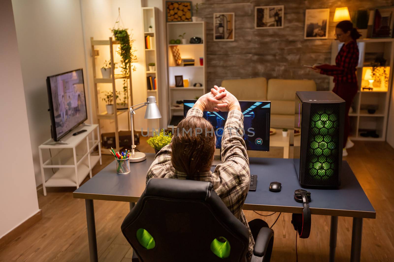 Back view of professional video gamer playing on powerful PC late at night in the living room.